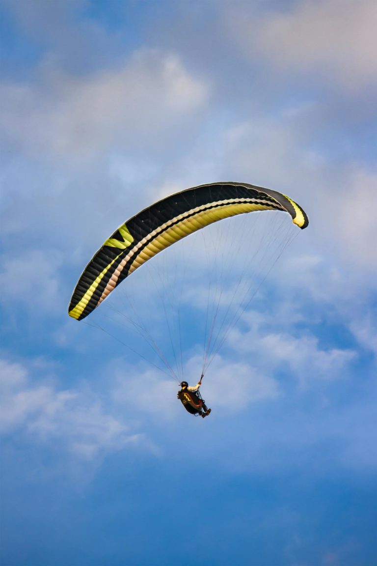 A paraglider soars through a vibrant blue sky with clouds, capturing the thrill of flight.