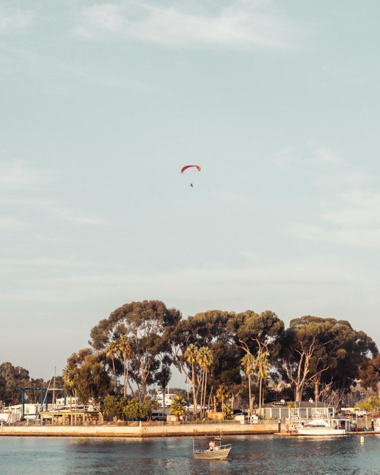 Scenic view of a paraglider soaring above Laguna Beach with a calm shoreline at sunset.