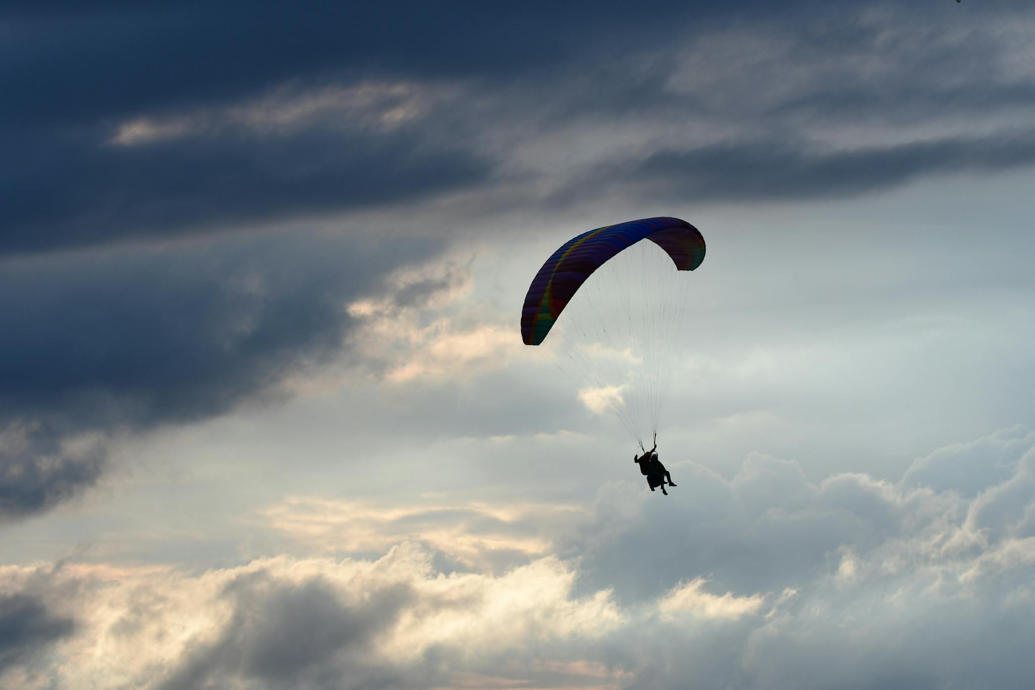 Silhouette of a paraglider soaring under dramatic clouds at dusk, capturing adventure and freedom.